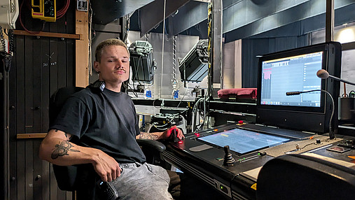 Foto zum Thema "Ausbildung zum Veranstaltungstechniker": Zu sehen ist Jakob, der in der Semperoper Dresden als Bühnenmaschinist arbeitet. Er sitzt im Kontrollraum, vor ihm zahlreiche Monitore und Mischpulte.