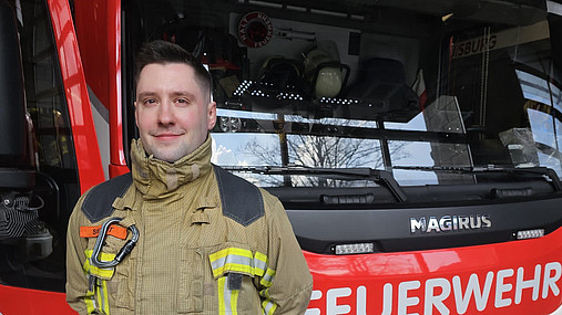 Foto zum Thema "Feuerwehrmann werden": Zu sehen ist Lucas, der vor einem Feuerwehrauto steht und im Jobkompass Einblicke in seinen Beruf gibt.